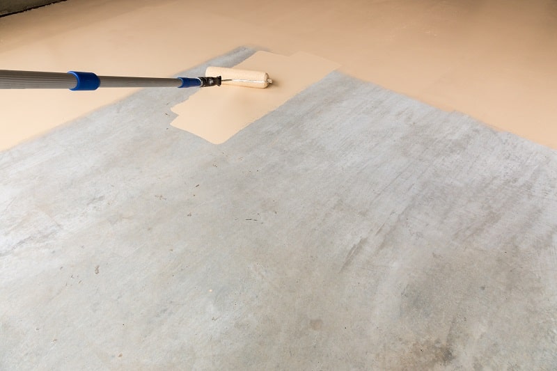 Worker Painting Floor of Garage with Roller.